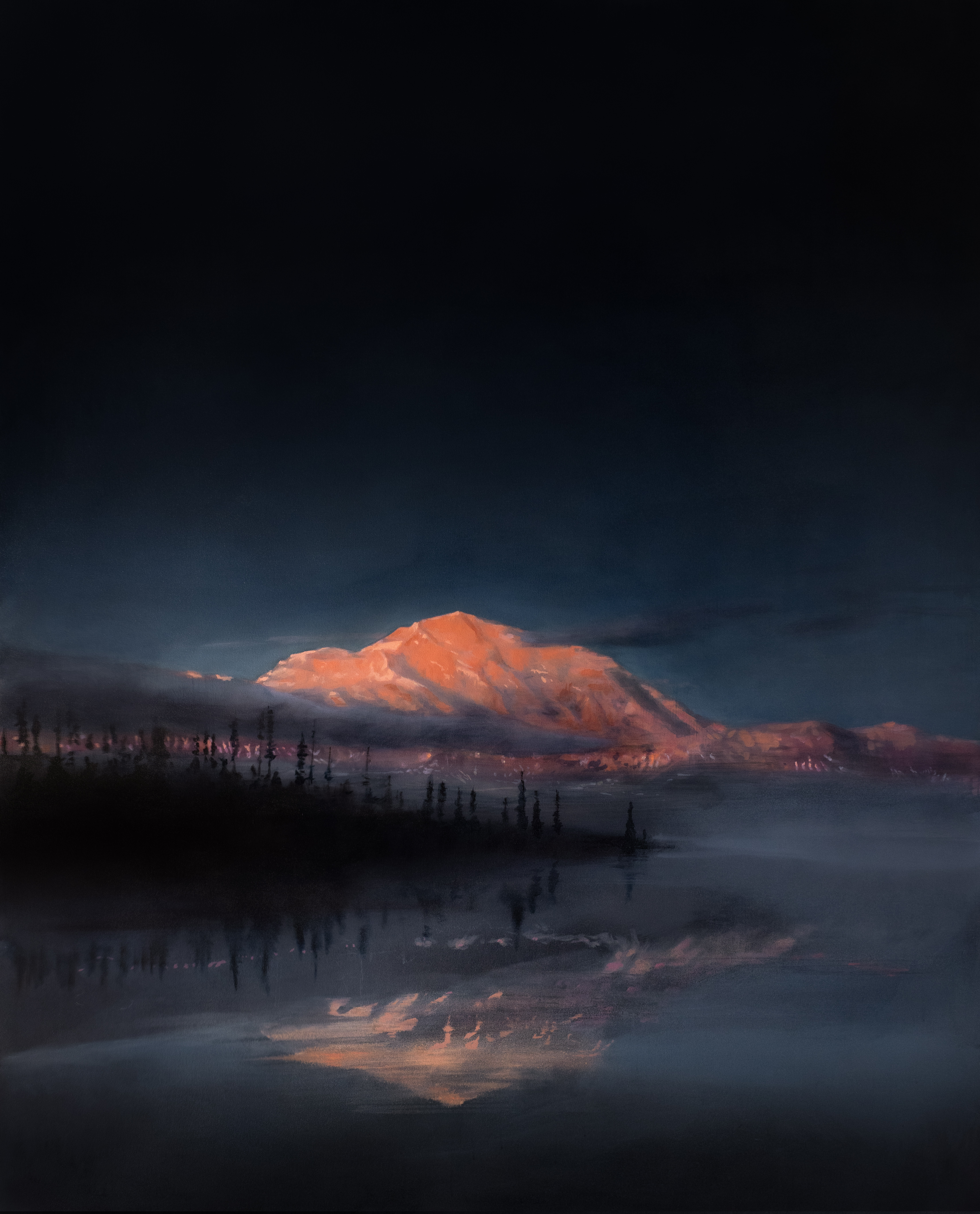 A snow-capped mountain peak glows in warm amber and orange tones against a deep blue twilight sky, its reflection mirrored in still water below. Silhouetted evergreen trees line the shoreline in the foreground, creating a stark contrast between the illuminated summit and the dark landscape.