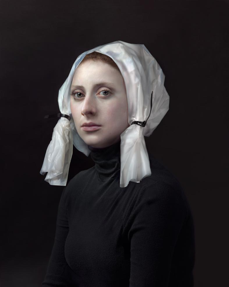 Portrait of a woman against a dark background, wearing a black turtleneck and a white linen head covering tied beneath the chin. Her gaze is directed slightly away from the camera, with a composed, contemplative expression.
