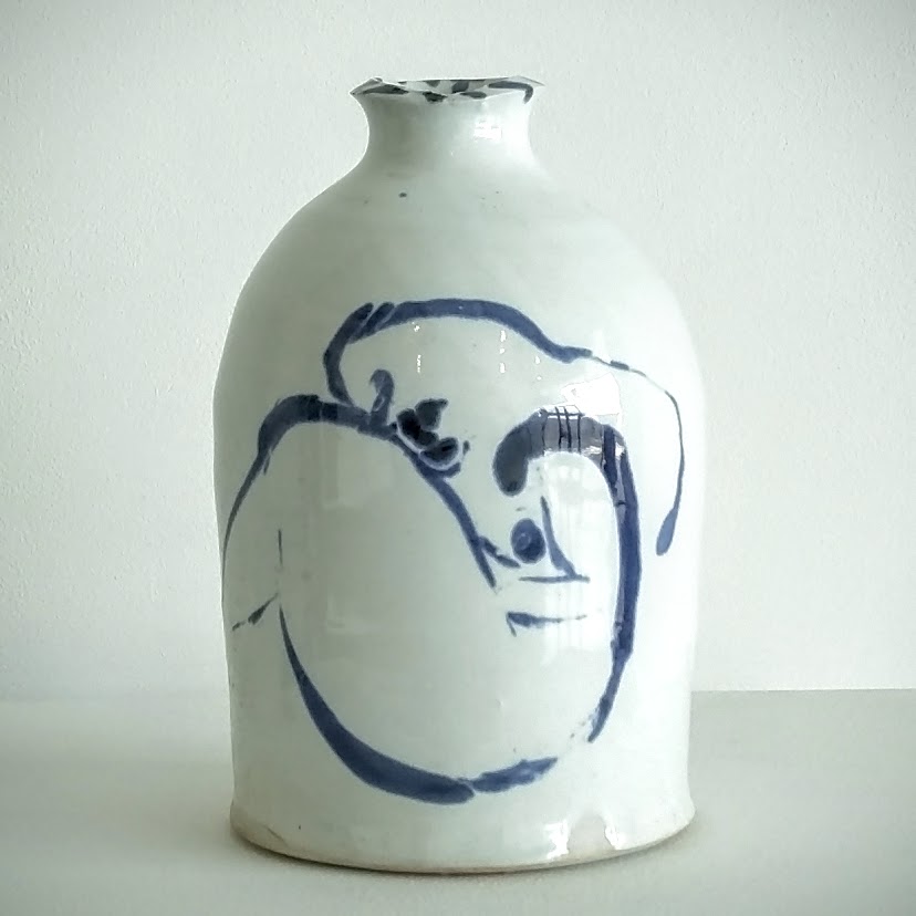 White porcelain bottle with a rounded body and narrow neck, decorated with a loose cobalt blue line drawing of an abstract human figure on the front surface.