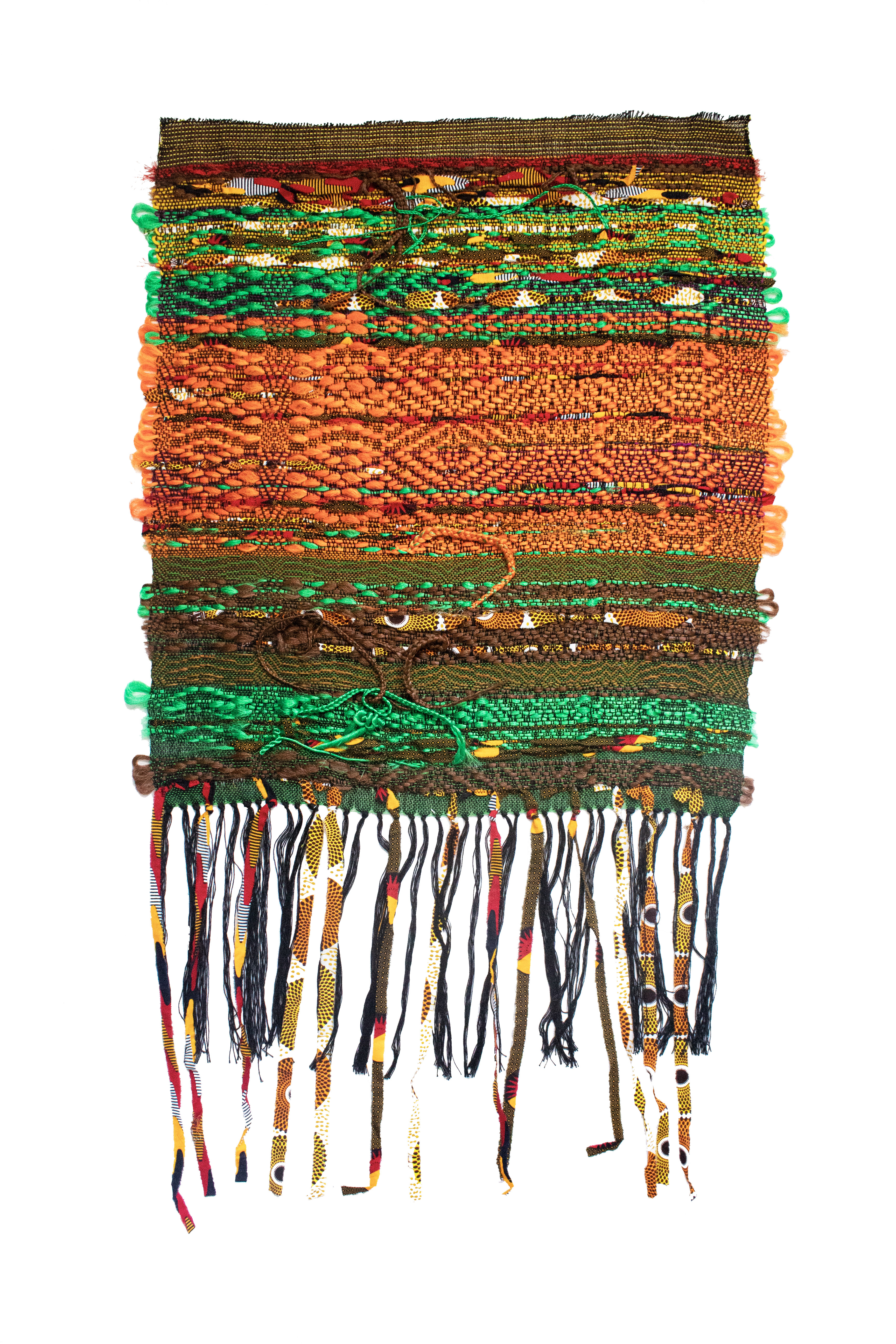 Layered horizontal bands of woven and textile materials in earthy tones of brown, orange, green, and gold, with decorative green pom-poms along the edges and multicolored braided fringe hanging from the bottom.