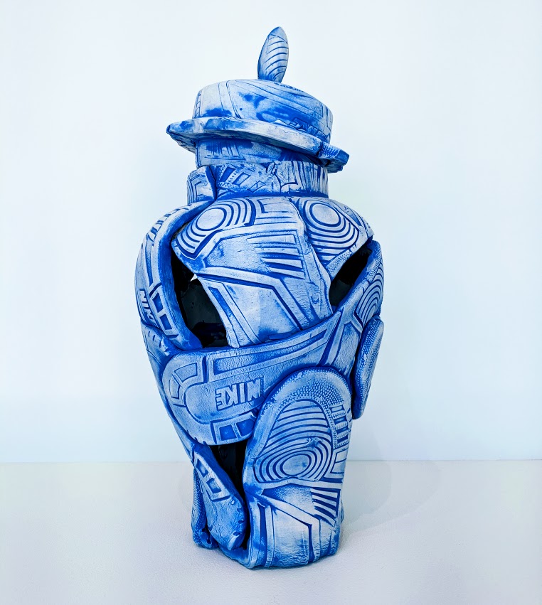 A blue and white porcelain vessel shaped like a deconstructed sneaker, decorated with geometric patterns and concentric circles in the style of Delft pottery. The form features an opening at the center with a lidded top piece, creating a sculptural object that merges functional vessel design with contemporary street culture imagery.