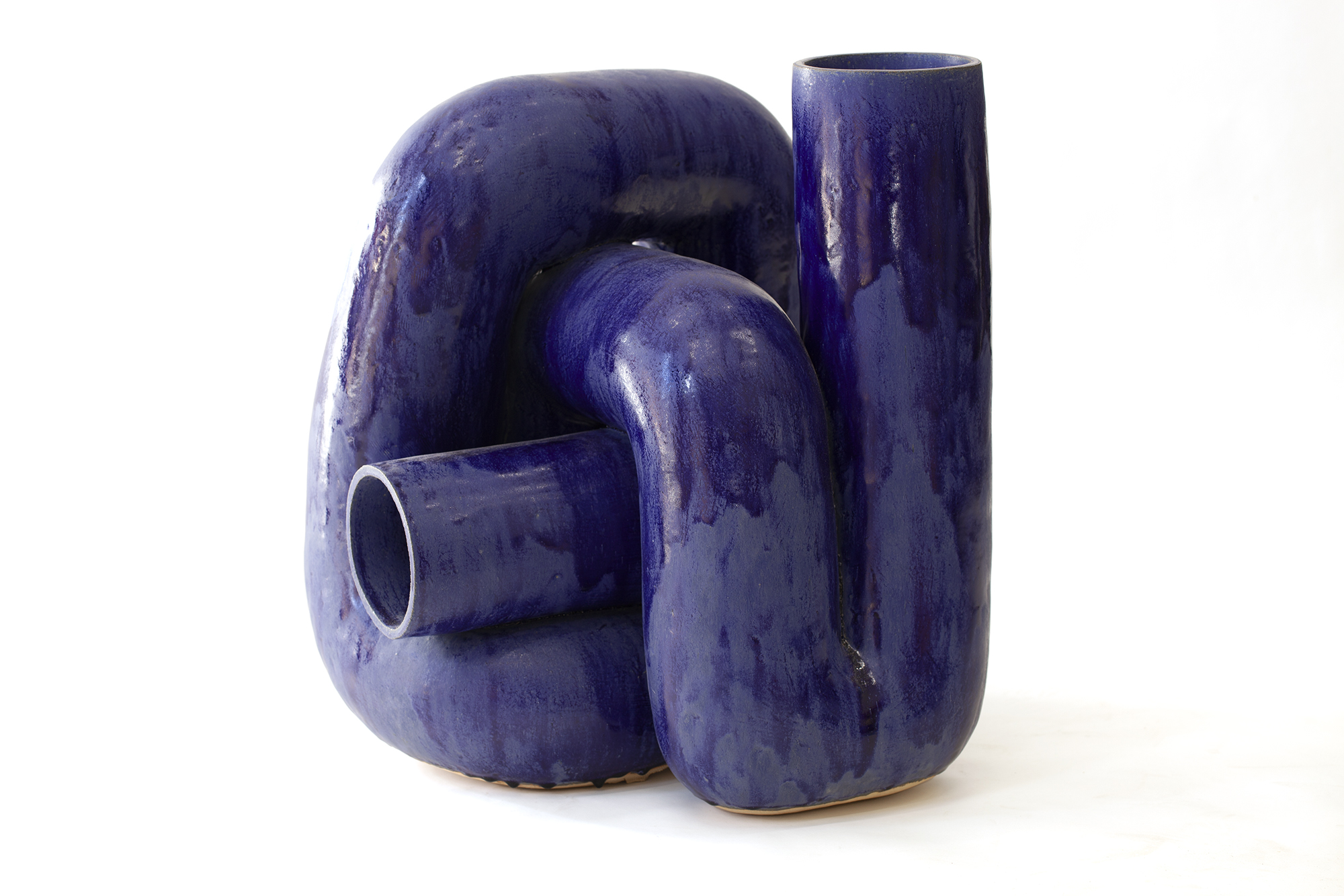 Three abstract ceramic vessels in deep blue glaze arranged in an organic cluster. The forms feature curved, interlocking shapes with smooth, flowing surfaces and glossy finishes, creating a sculptural composition with negative spaces and openings between the elements.