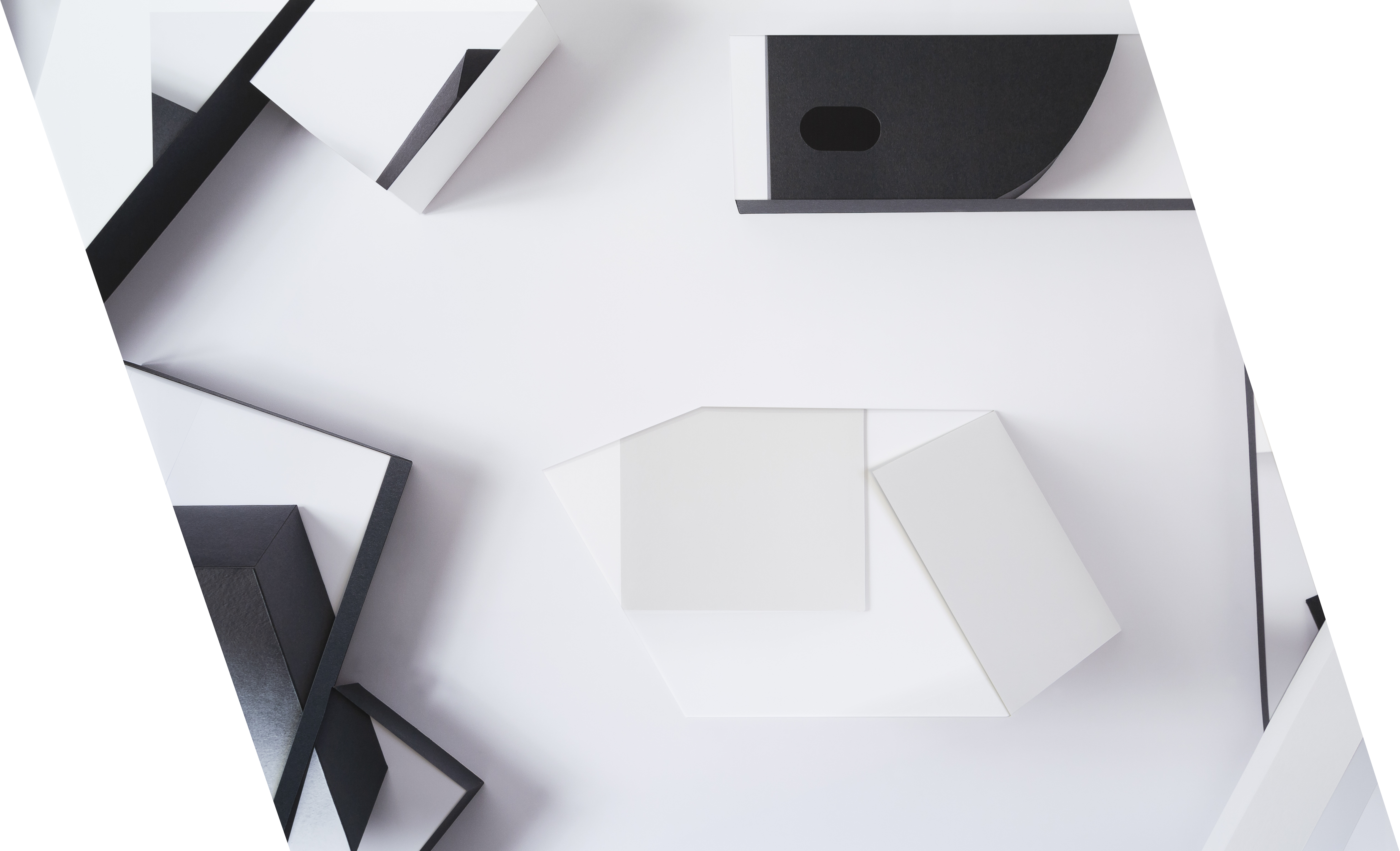 Geometric abstract composition of layered white and black paper forms arranged against a white surface, creating sharp angular shapes and shadows that suggest depth and three-dimensionality through careful arrangement and light.