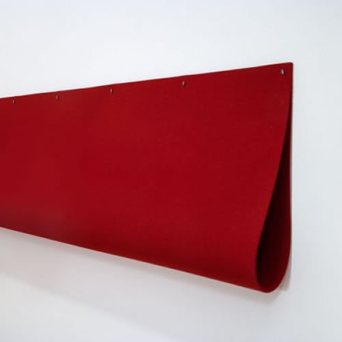 A deep red industrial felt panel mounted horizontally against a white wall, its right edge folded dramatically downward in a sharp crease, creating a three-dimensional sculptural form that casts subtle shadows.