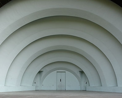A series of concentric white arched structures recede toward a distant doorway in the center, creating a tunnel-like perspective. The geometric composition emphasizes depth and symmetry through repeated curved architectural forms against a minimal, monochromatic interior space.