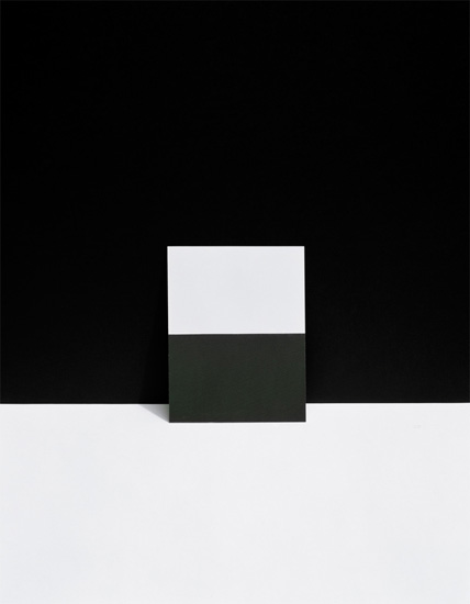 A geometric composition divided by a dark horizontal band, with a light gray rectangular form positioned above against a black background, and a lighter gray section below, creating a stark, minimalist arrangement of overlapping planes and tonal contrasts.