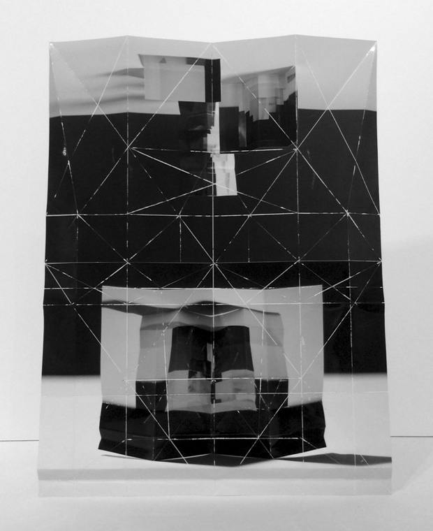 Black and white folded and layered printed paper construction featuring geometric line drawings overlaid on architectural imagery, creating a three-dimensional collage with alternating planes of transparent and opaque sections that reveal fragmented views of urban buildings.