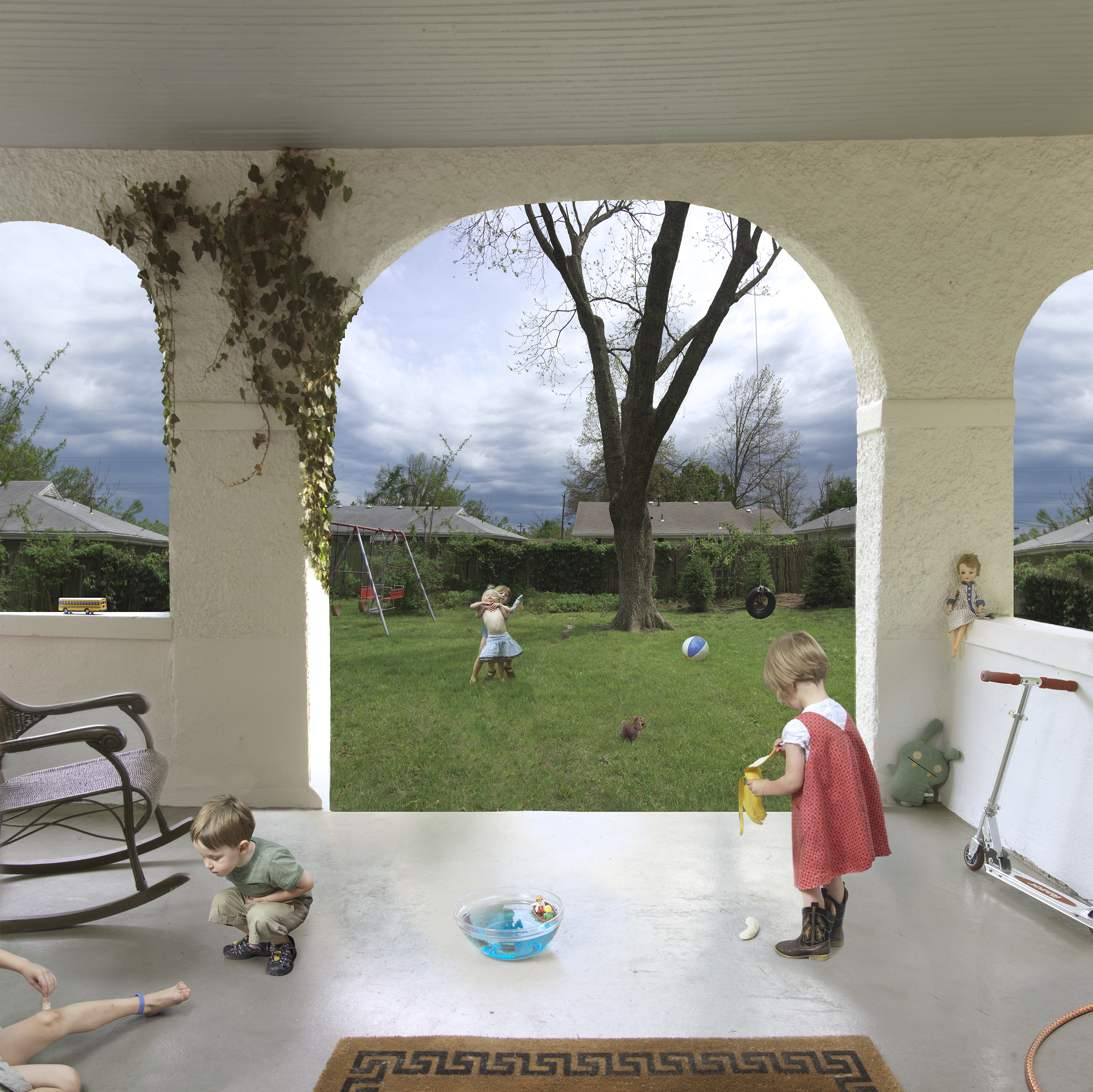A covered patio with white columns frames a backyard scene where several young children play on a sunny lawn. In the foreground, children engage in various activities on the concrete floor—one crouches near a blue toy basin, another holds a banana—while others play ball and swing from a tire in the grassy yard beyond. Dark storm clouds gather in the sky above the manicured suburban landscape, creating atmospheric contrast with the bright daylit scene.