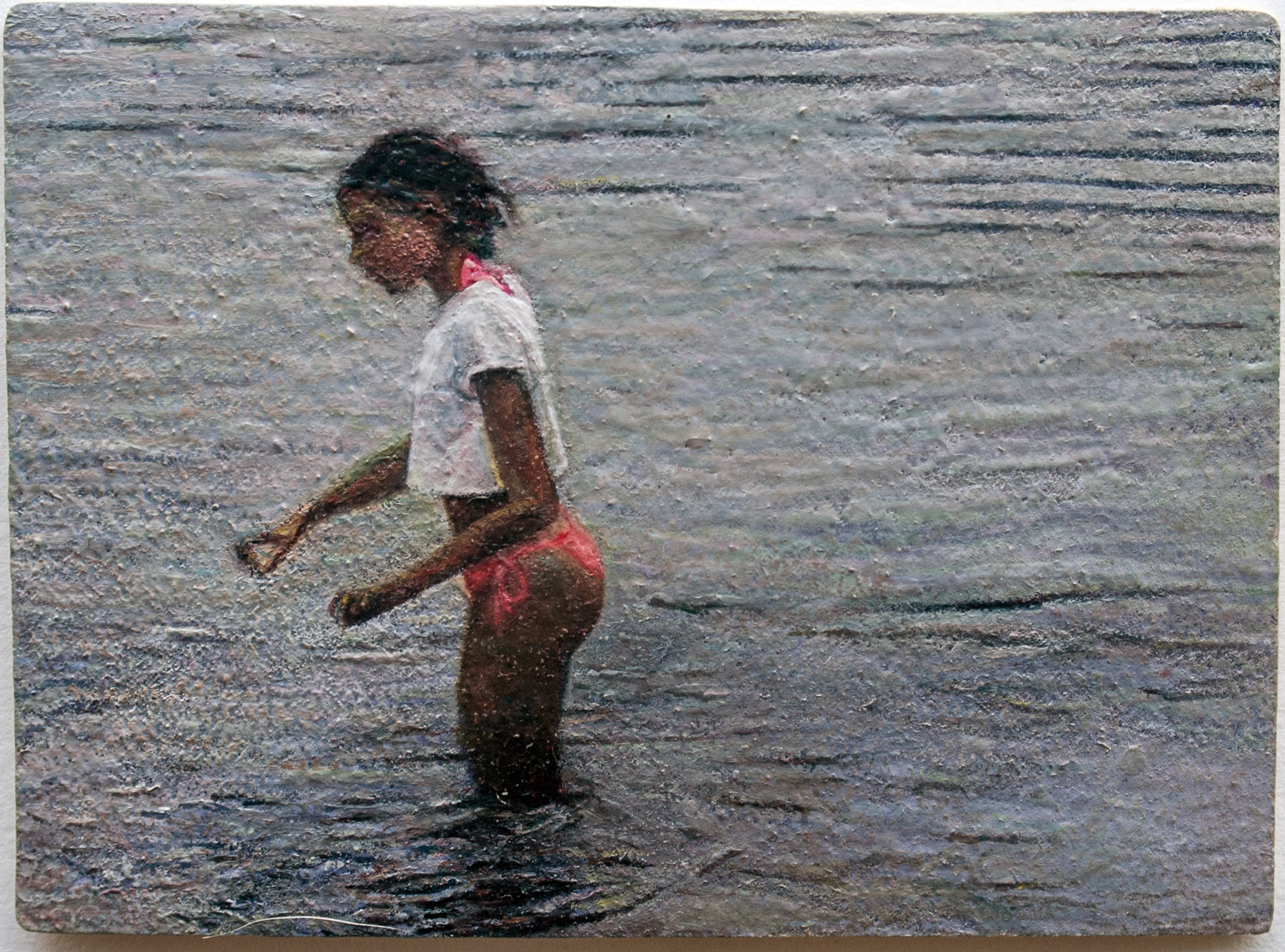 A young figure in a white t-shirt and red shorts stands in shallow water, viewed from the side in profile. The figure has dark hair pulled back with a pink headband and appears to be in motion or gesturing. The water and background are rendered in muted tones of gray and blue-green, with a textured, layered quality that suggests mixed media application.