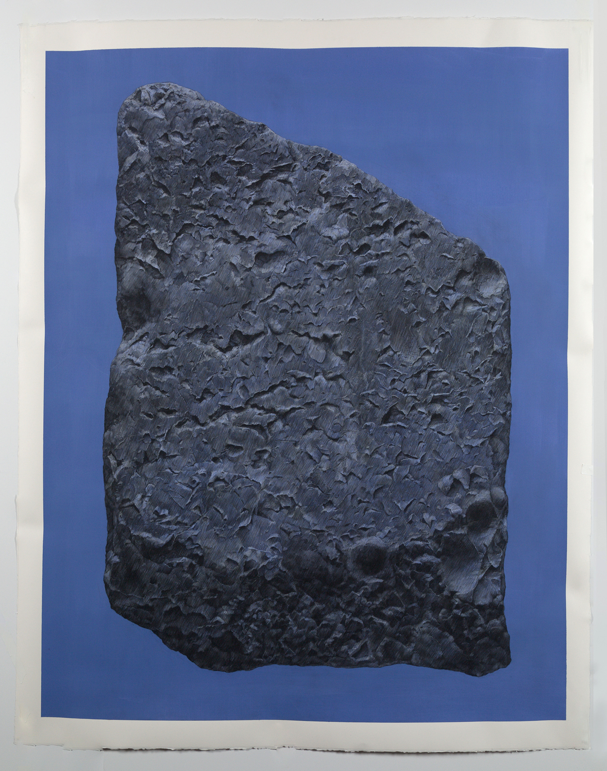 A dark gray textured stone fragment positioned vertically against a deep blue background, its rough surface densely carved with linear marks and patterns that create an intricate, weathered appearance.