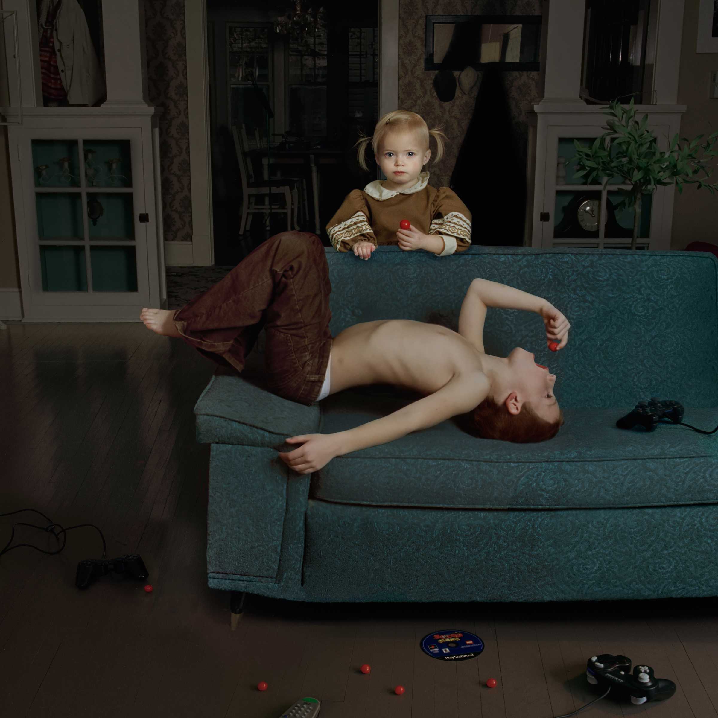 A young woman lies sprawled across a teal upholstered sofa in an elegantly furnished living room, her legs draped over the armrest, while a small child in brown clothing stands on the cushions beside her. Red spheres are scattered across the dark wooden floor, along with gaming controllers and a DVD case, creating a playful domestic scene rendered in rich, saturated colors.
