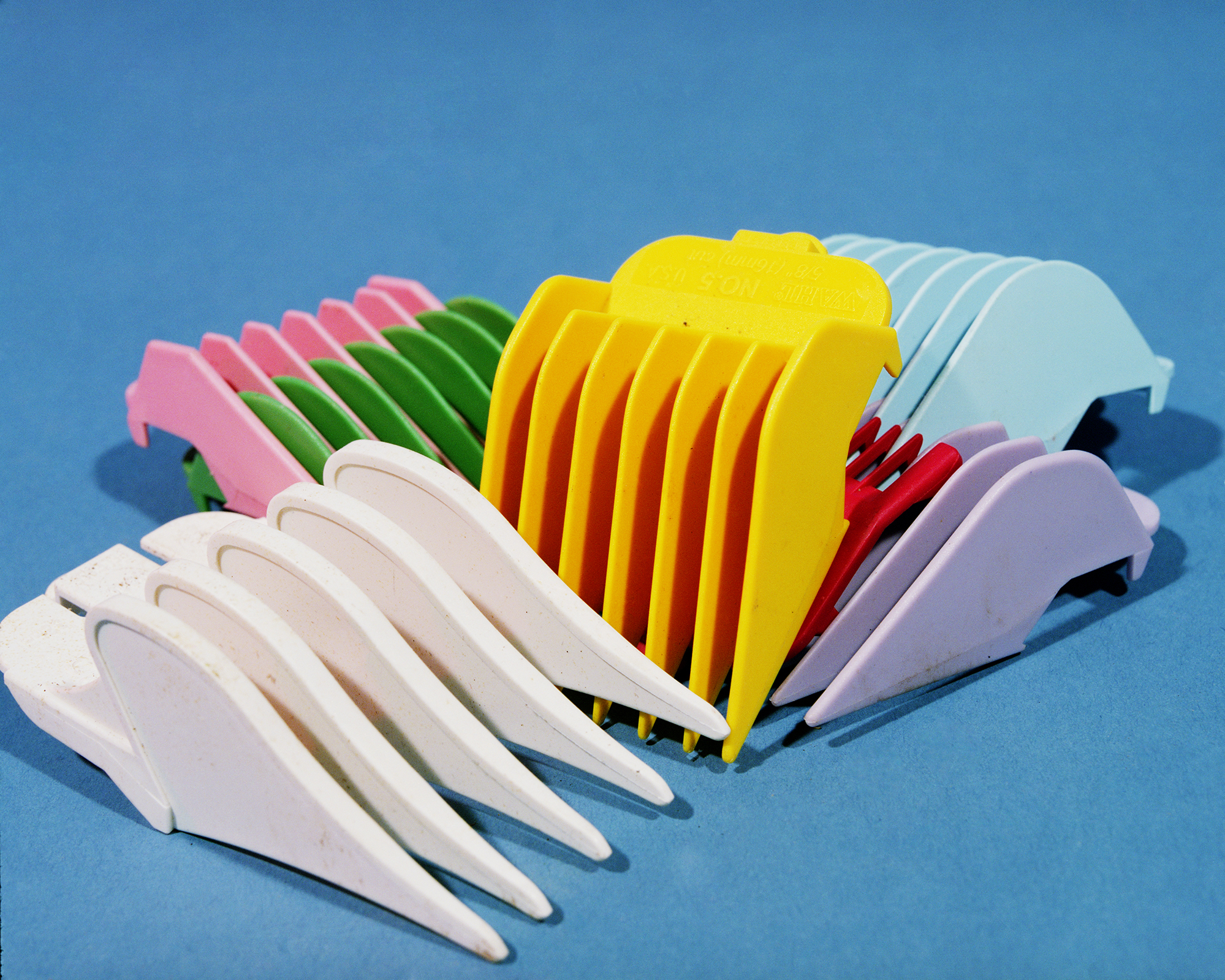 Colorful plastic hair clips arranged in overlapping rows against a bright blue background, displaying shades of white, pink, green, yellow, red, light blue, and purple in a playful still-life composition.