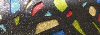 Dark background densely covered with multicolored glitter and sparkles in shades of blue, red, yellow, and gold, interspersed with organic, elongated forms suggesting anatomical or botanical structures in muted tones.
