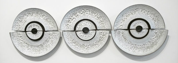 Three circular cast concrete or plaster discs arranged in a horizontal row, each featuring a textured surface with a central circular opening and concentric ring detail, creating a rhythmic, minimalist composition in monochromatic gray tones.