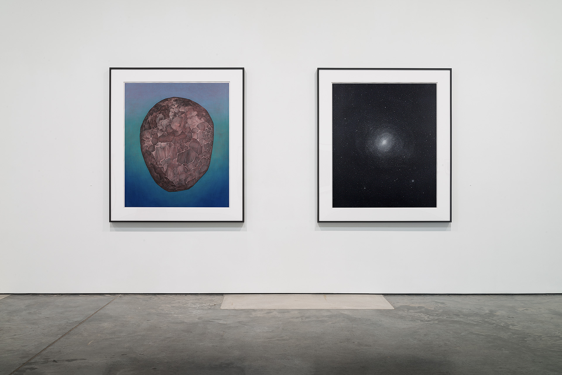 Two framed artworks hung side by side on a gallery wall: at left, a textured brown spherical form rendered in layered materials against a gradient blue background; at right, a luminous spiral galaxy depicted in precise detail against a black starfield.