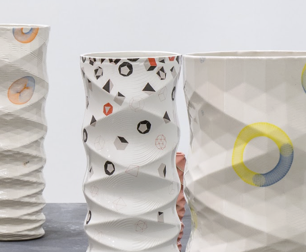 Three ceramic vessels with undulating white surfaces decorated with geometric patterns in black, red, and yellow. The forms feature wavy, rippled walls and circular graphic elements, displayed against a neutral background.