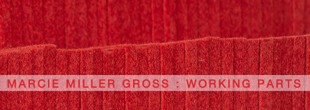 Stacked layers of deep red industrial felt arranged horizontally, creating a textured composition of varying tones and densities. A pale banner with embossed text runs across the center, emphasizing the work's material weight and compressed surface.