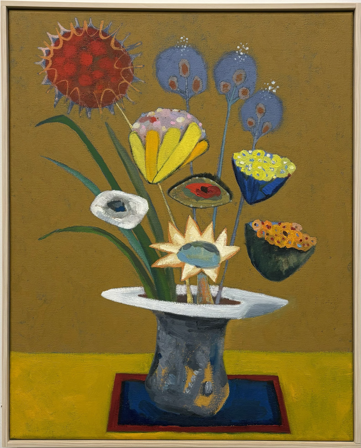 Whimsical still life featuring an array of imaginative flowers and botanical forms in a dark vessel against a mustard and yellow background. The composition includes surreal blooms with eye-like centers in shades of red, white, yellow, and blue, arranged in a playful, dreamlike arrangement that blurs the line between flora and abstraction.
