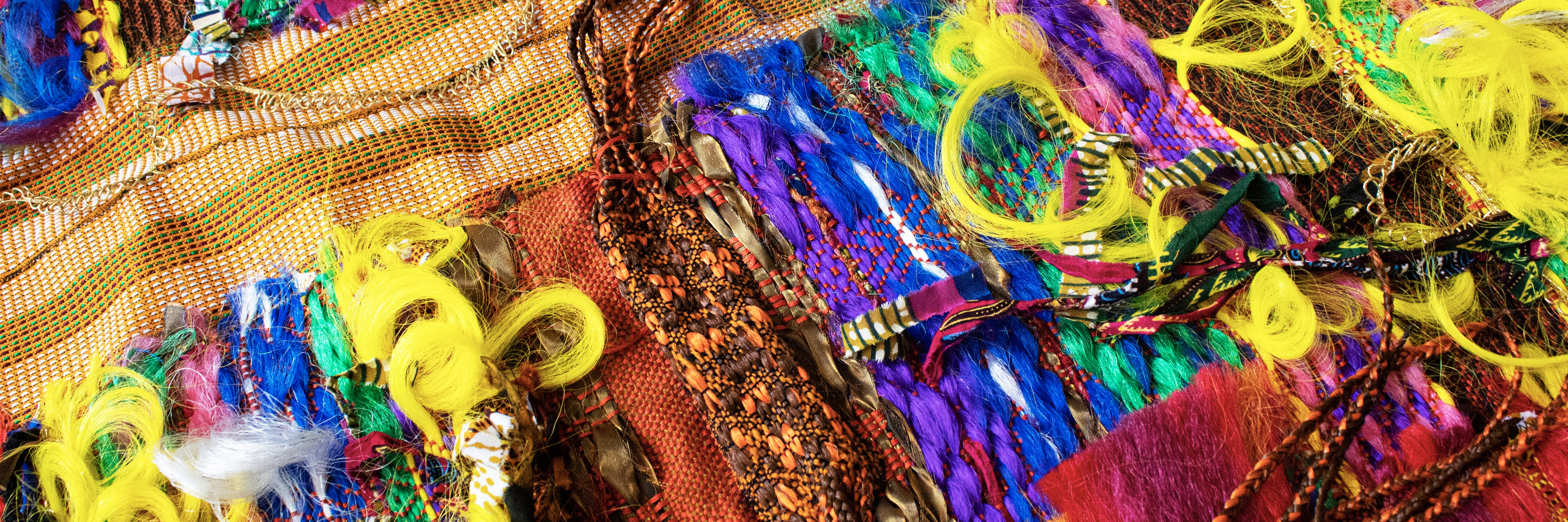 Vibrant textile artwork featuring intricately woven and braided synthetic hair in bold colors including yellow, blue, purple, pink, and orange, layered over patterned fabrics with geometric designs and mesh textures, creating a dense, three-dimensional composition that celebrates African diaspora aesthetics and hair culture.