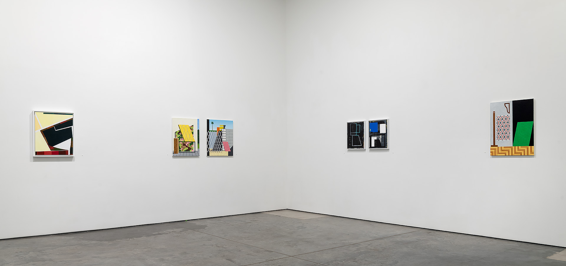 Gallery installation view showing five framed artworks arranged across a white wall above a gray floor. The works feature geometric compositions with bold colors including yellow, black, blue, green, and red, employing collage techniques and constructed spatial elements characteristic of contemporary abstract and architectural-influenced painting.